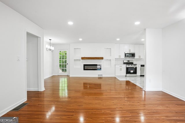 unfurnished living room featuring a notable chandelier, a glass covered fireplace, wood finished floors, and visible vents
