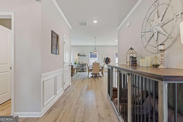 corridor featuring visible vents, light wood finished floors, ornamental molding, and a wainscoted wall