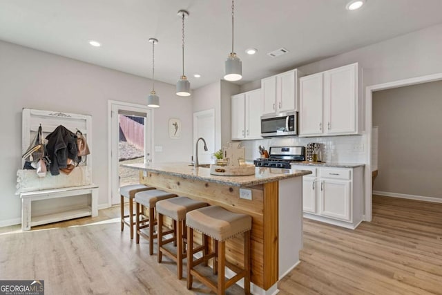 kitchen with white cabinets, visible vents, baseboards, an island with sink, and appliances with stainless steel finishes