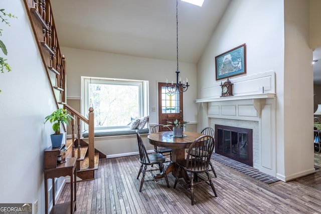 dining area with baseboards, an inviting chandelier, a brick fireplace, hardwood / wood-style floors, and high vaulted ceiling