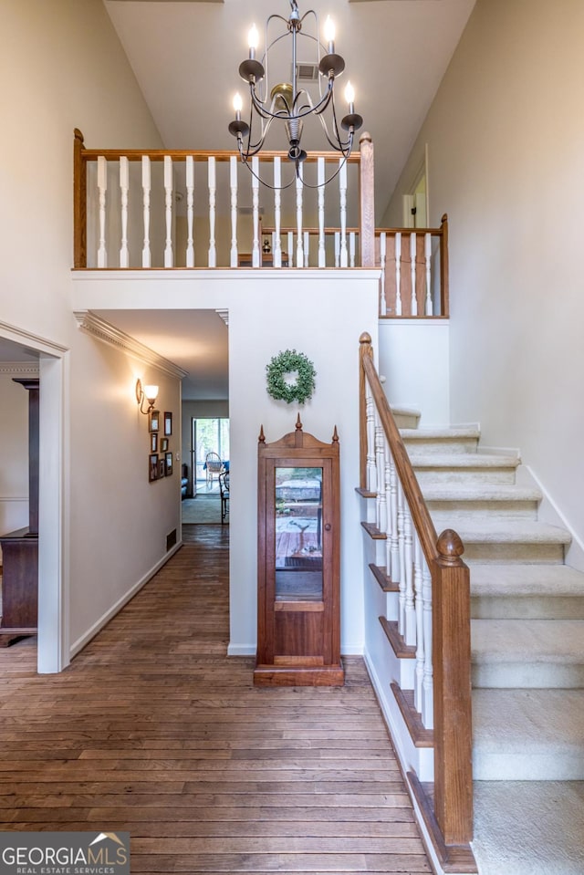 stairway with wood finished floors, a high ceiling, baseboards, and a notable chandelier
