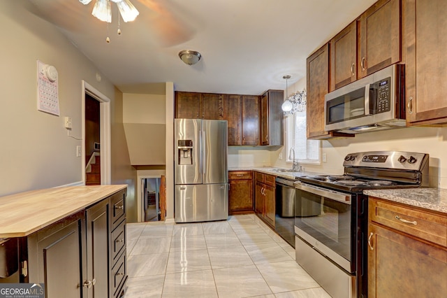 kitchen featuring stainless steel appliances, a sink, butcher block counters, decorative light fixtures, and ceiling fan