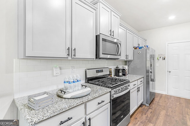 kitchen with light stone countertops, stainless steel appliances, wood finished floors, and decorative backsplash