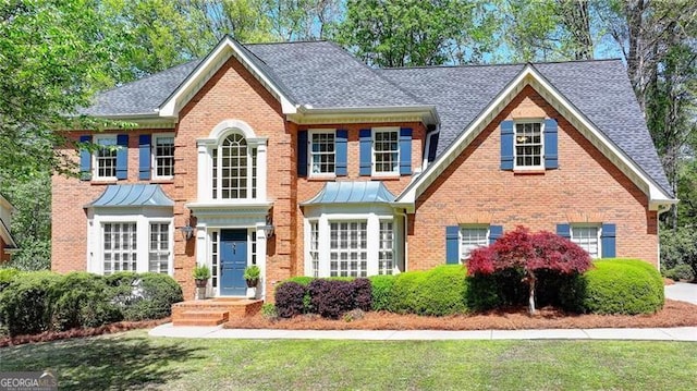 view of front of property featuring brick siding, a shingled roof, and a front yard