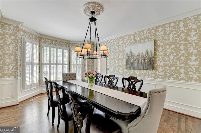 dining area with wainscoting, wallpapered walls, an inviting chandelier, and crown molding