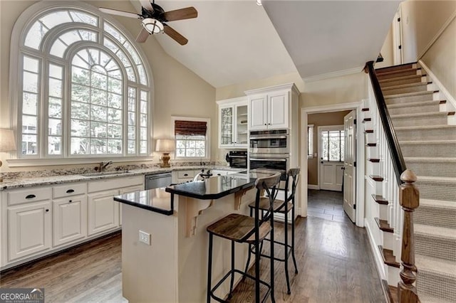 kitchen with white cabinets, stainless steel appliances, a kitchen bar, a ceiling fan, and wood finished floors