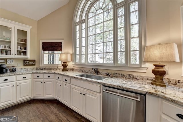 kitchen featuring vaulted ceiling, stainless steel dishwasher, a sink, glass insert cabinets, and white cabinetry