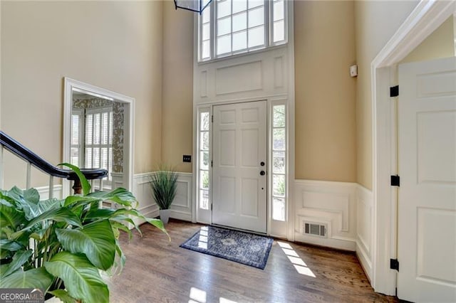 foyer featuring a decorative wall, a towering ceiling, a healthy amount of sunlight, and visible vents