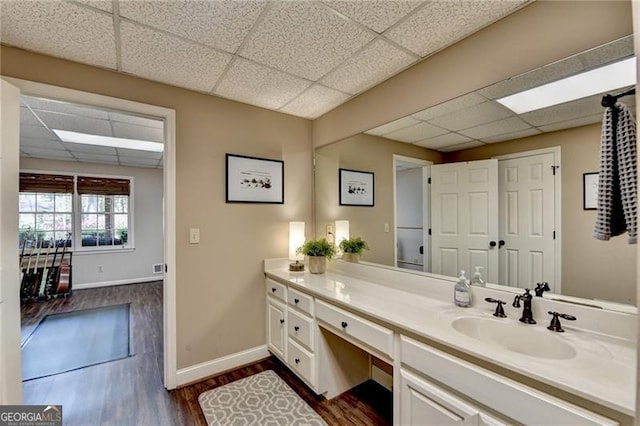 bathroom with a paneled ceiling, vanity, baseboards, and wood finished floors