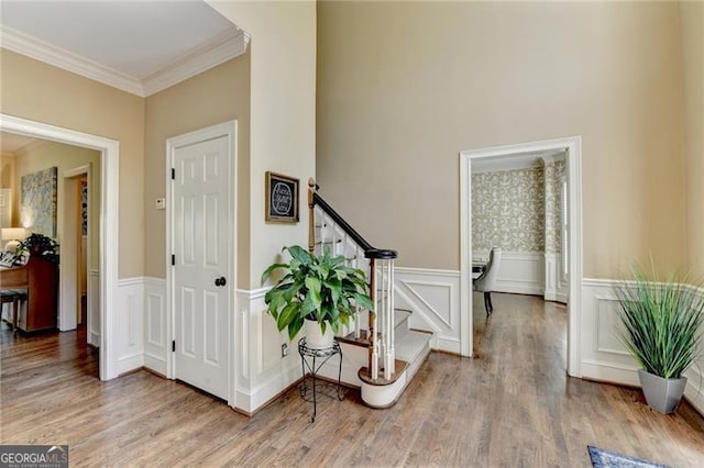 entryway with a wainscoted wall, wood finished floors, stairway, a decorative wall, and ornamental molding