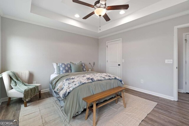 bedroom with a tray ceiling, wood finished floors, baseboards, and recessed lighting