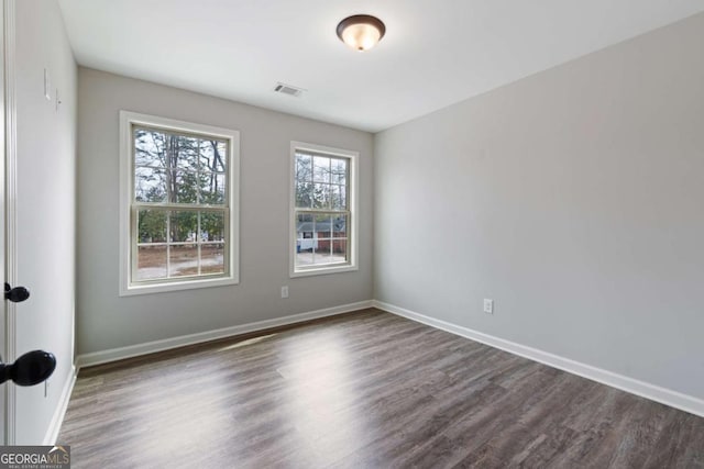 empty room featuring baseboards, dark wood-style flooring, and visible vents