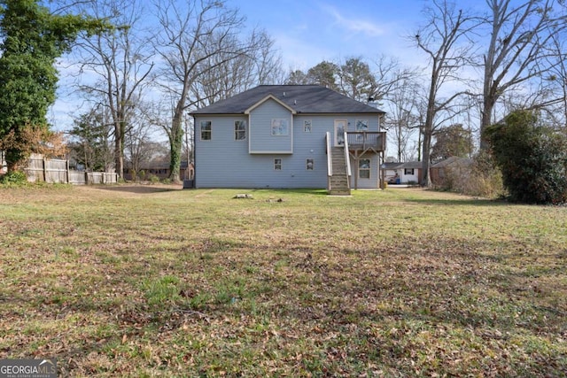 rear view of property featuring fence, a wooden deck, a lawn, and stairway