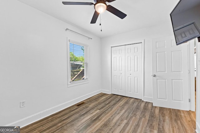 unfurnished bedroom featuring wood finished floors, a closet, ceiling fan, baseboards, and visible vents