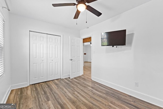 unfurnished bedroom with wood finished floors, a closet, baseboards, and ceiling fan