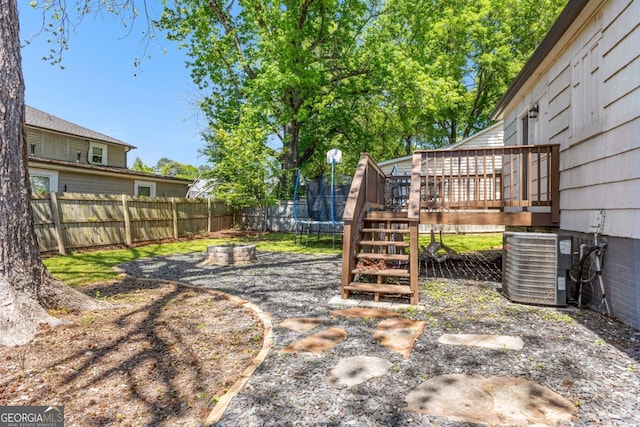 view of yard with a trampoline, a fenced backyard, cooling unit, and a deck