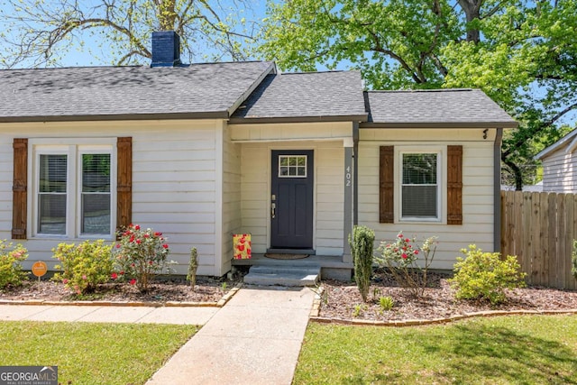 view of front of property with a chimney, fence, a shingled roof, and a front yard
