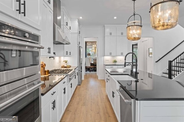 kitchen with wall chimney range hood, dark countertops, a sink, stainless steel appliances, and recessed lighting