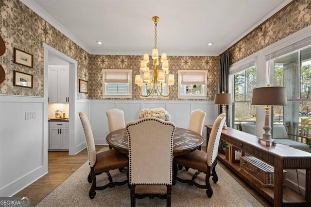 dining area featuring wainscoting, an inviting chandelier, wallpapered walls, wood finished floors, and crown molding