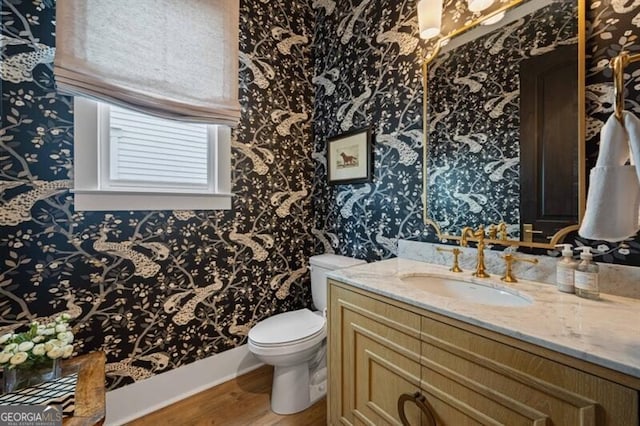 bathroom featuring toilet, vanity, wood finished floors, and wallpapered walls