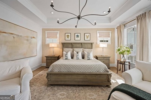 bedroom featuring a tray ceiling, wood finished floors, ornamental molding, baseboards, and a notable chandelier
