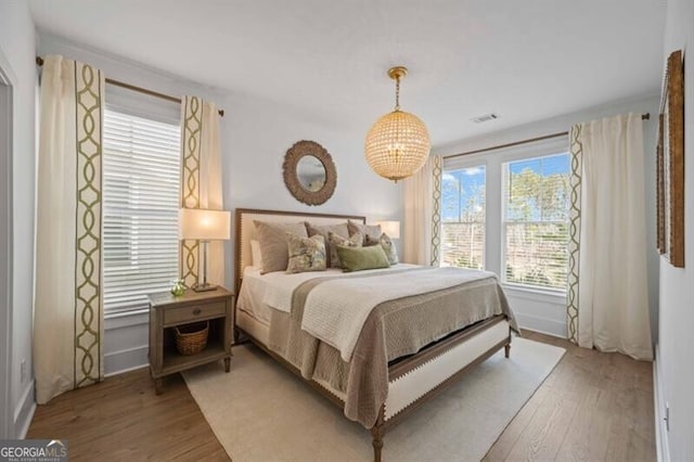 bedroom with baseboards, a chandelier, wood finished floors, and visible vents