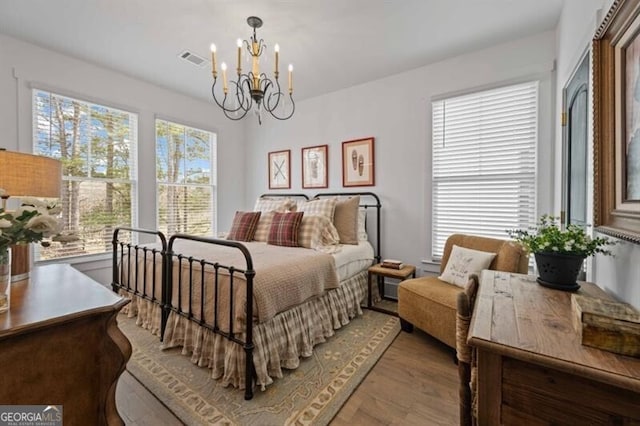 bedroom featuring wood finished floors, visible vents, and a notable chandelier