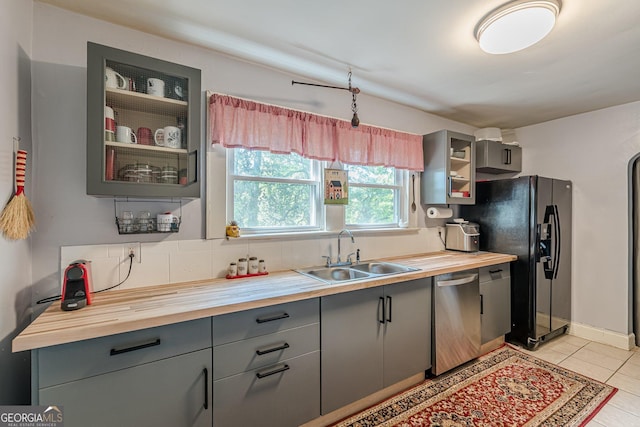 kitchen with a sink, wooden counters, dishwasher, gray cabinetry, and black fridge
