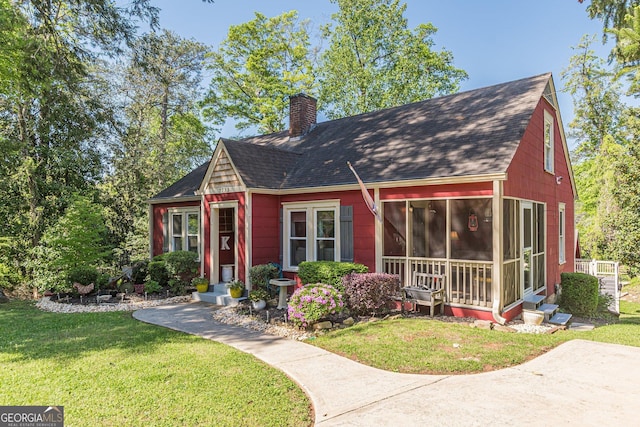view of front facade featuring a chimney, a sunroom, a shingled roof, and a front yard