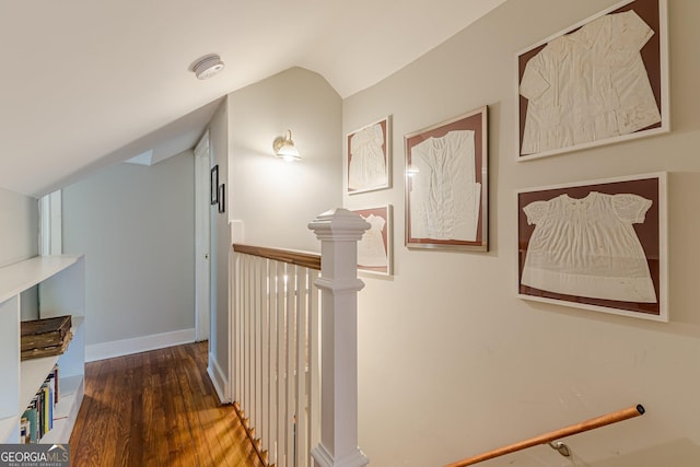 corridor with vaulted ceiling, wood finished floors, and an upstairs landing