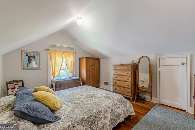 bedroom with dark wood-type flooring, vaulted ceiling, and visible vents
