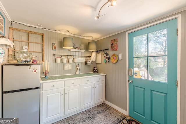 kitchen with light countertops, ornamental molding, freestanding refrigerator, baseboards, and white cabinetry