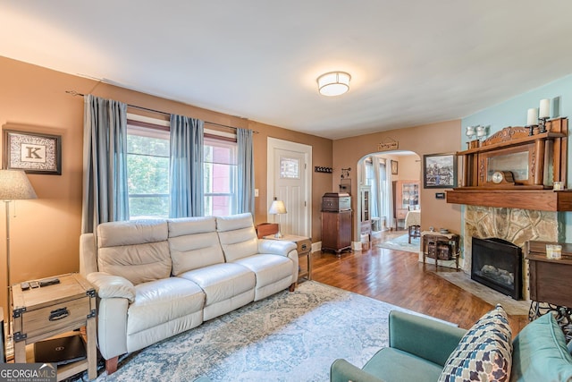 living room featuring a stone fireplace, arched walkways, wood finished floors, and baseboards