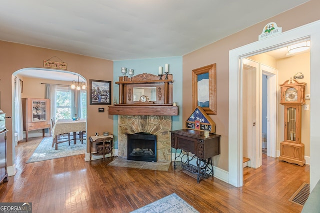 living room with arched walkways, baseboards, visible vents, hardwood / wood-style flooring, and a fireplace