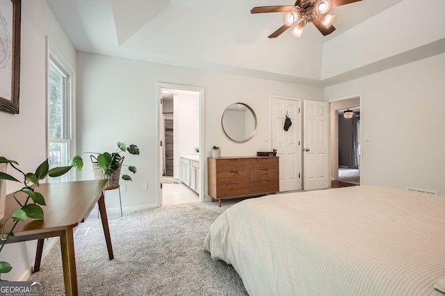bedroom with a raised ceiling, baseboards, ensuite bath, and light colored carpet