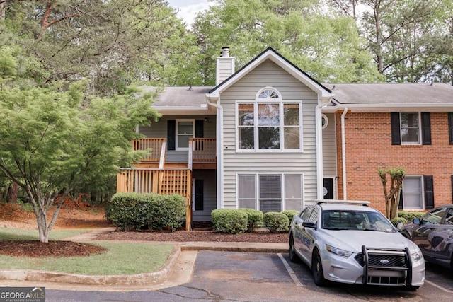 view of front of house featuring a chimney, uncovered parking, and view of scattered trees
