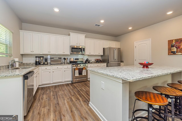 kitchen featuring a kitchen breakfast bar, a sink, stainless steel appliances, dark wood-style flooring, and visible vents
