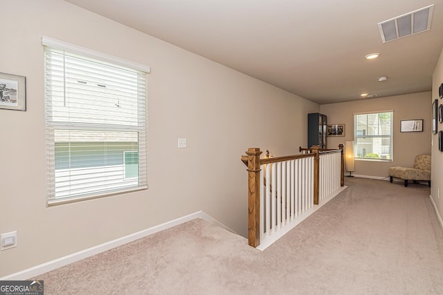 hall with baseboards, visible vents, carpet, and an upstairs landing