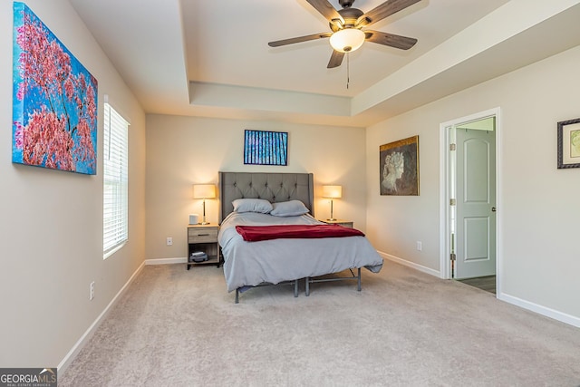 carpeted bedroom with ceiling fan, baseboards, and a raised ceiling