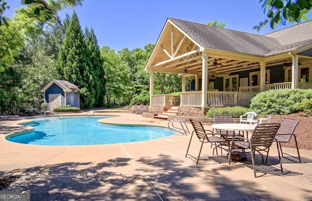 outdoor pool with a patio area, a ceiling fan, a storage unit, and an outbuilding