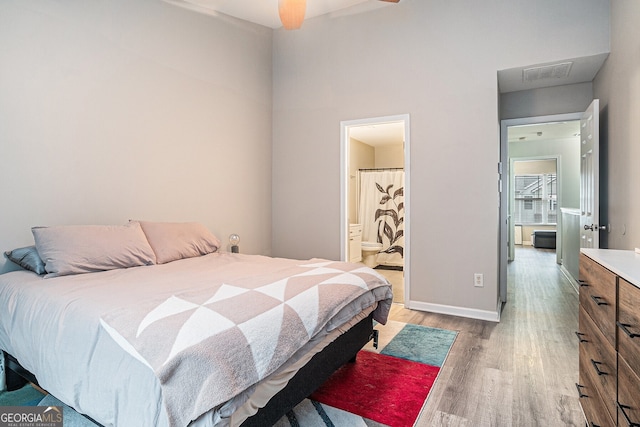 bedroom with baseboards, light wood-style flooring, visible vents, and connected bathroom