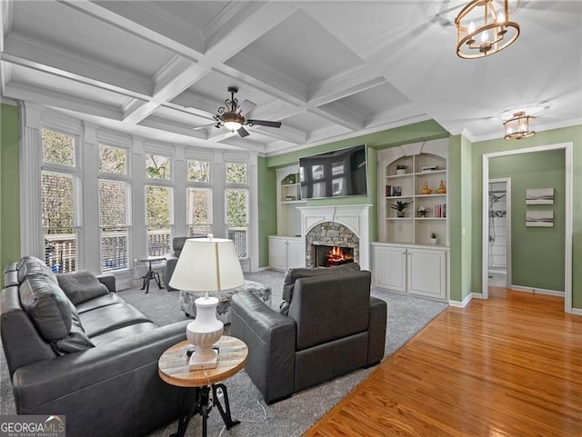 living area featuring crown molding, wood finished floors, a stone fireplace, beamed ceiling, and baseboards