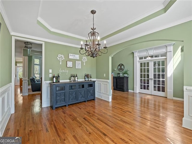 dining room with a tray ceiling, light wood-style floors, ornamental molding, and french doors