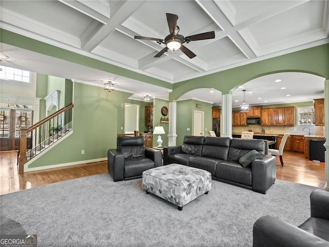living area with light wood-type flooring, ornamental molding, arched walkways, and ceiling fan