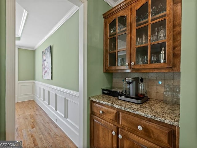 bar featuring decorative backsplash, light wood-style flooring, a wainscoted wall, and crown molding