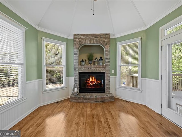 unfurnished living room featuring wainscoting, visible vents, lofted ceiling, wood finished floors, and a fireplace