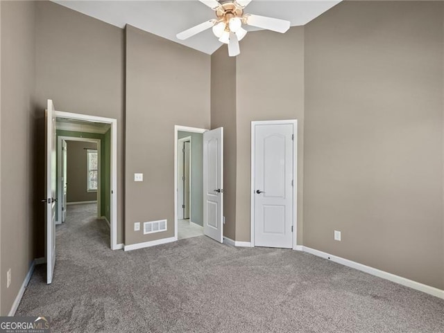 unfurnished bedroom featuring baseboards, carpet, visible vents, ceiling fan, and high vaulted ceiling