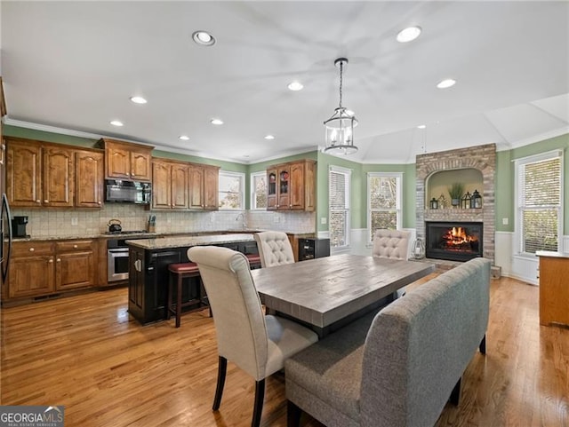 dining room featuring light wood-style flooring, ornamental molding, a brick fireplace, and plenty of natural light