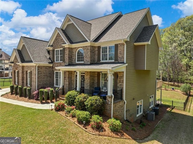 craftsman-style house with fence, covered porch, a front yard, and central AC unit
