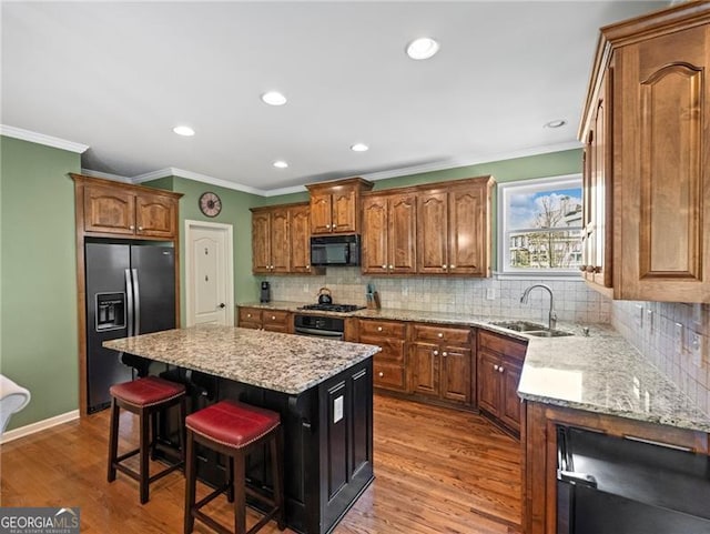 kitchen with a sink, black microwave, a breakfast bar, refrigerator with ice dispenser, and a kitchen island